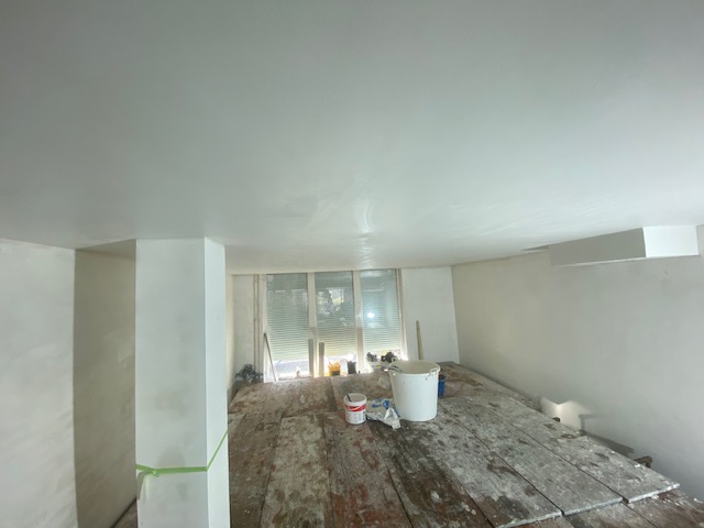Vers gestuukte zolderkamer: egaal wit plafond en witte wanden, met steigerplanken op de vloer